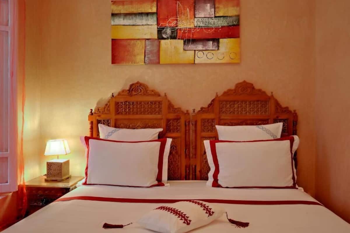 A double bed with a wooden headboard, two white pillows, and a red accent.
