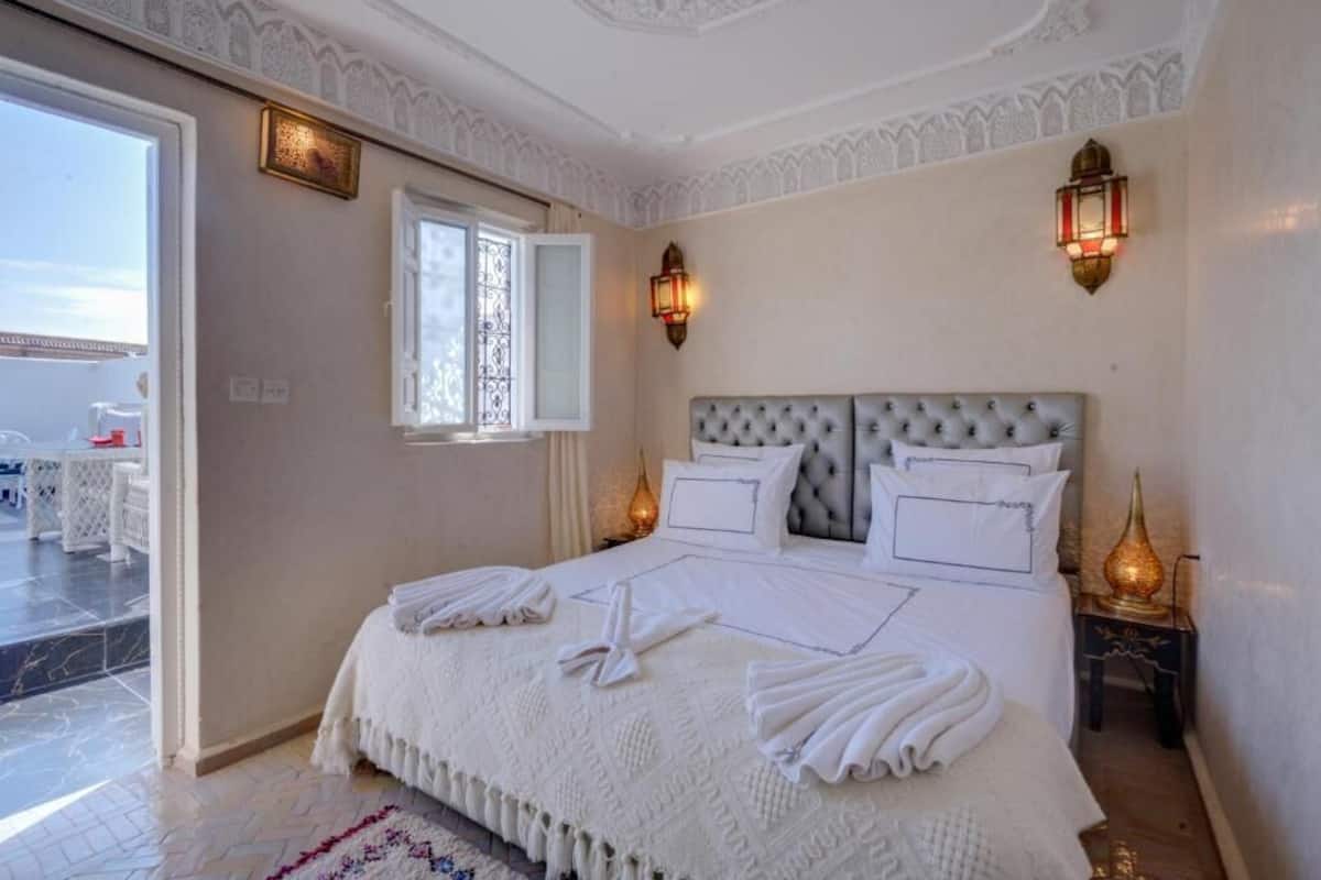 A bedroom with a large bed, two wall sconces, a window, and a view of the outside.