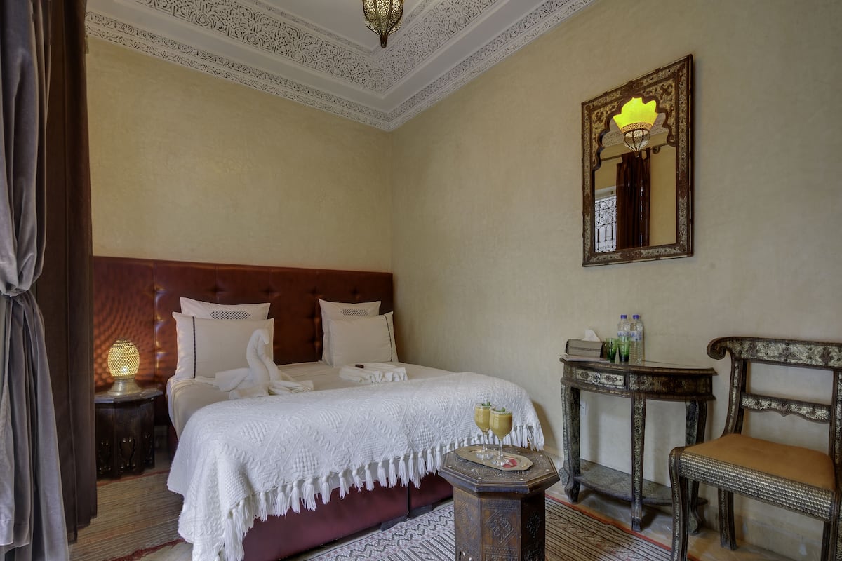 A hotel room with a large bed, a small table with a lamp, a chair, and a mirror on the wall.