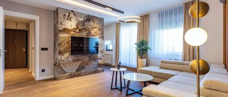 A modern living room with a stone fireplace, a sofa set, a TV mounted on the wall, and a floor lamp.