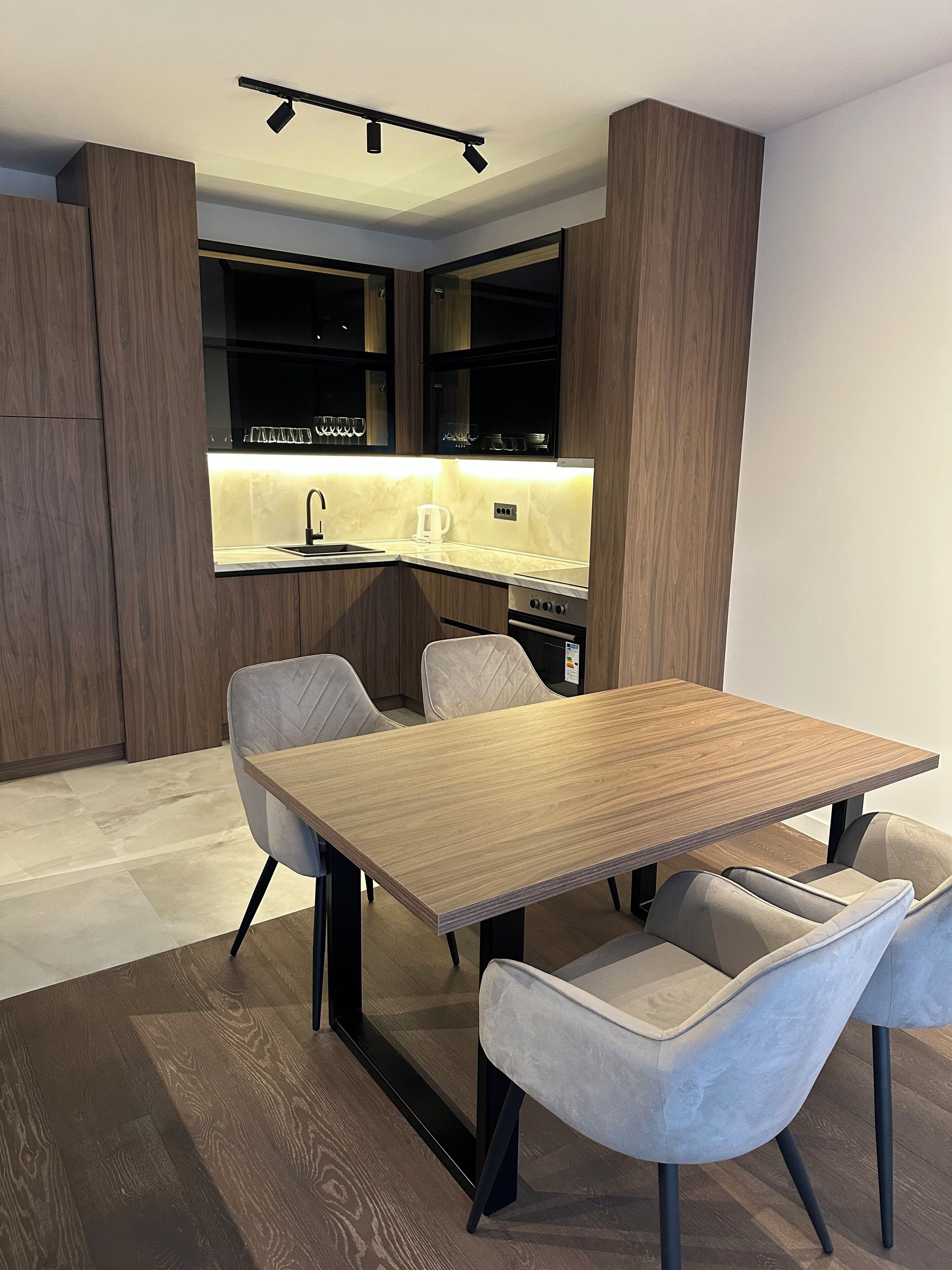 A modern kitchen with a built-in island, dark wood cabinetry, and a dining area with a wooden table and two chairs.