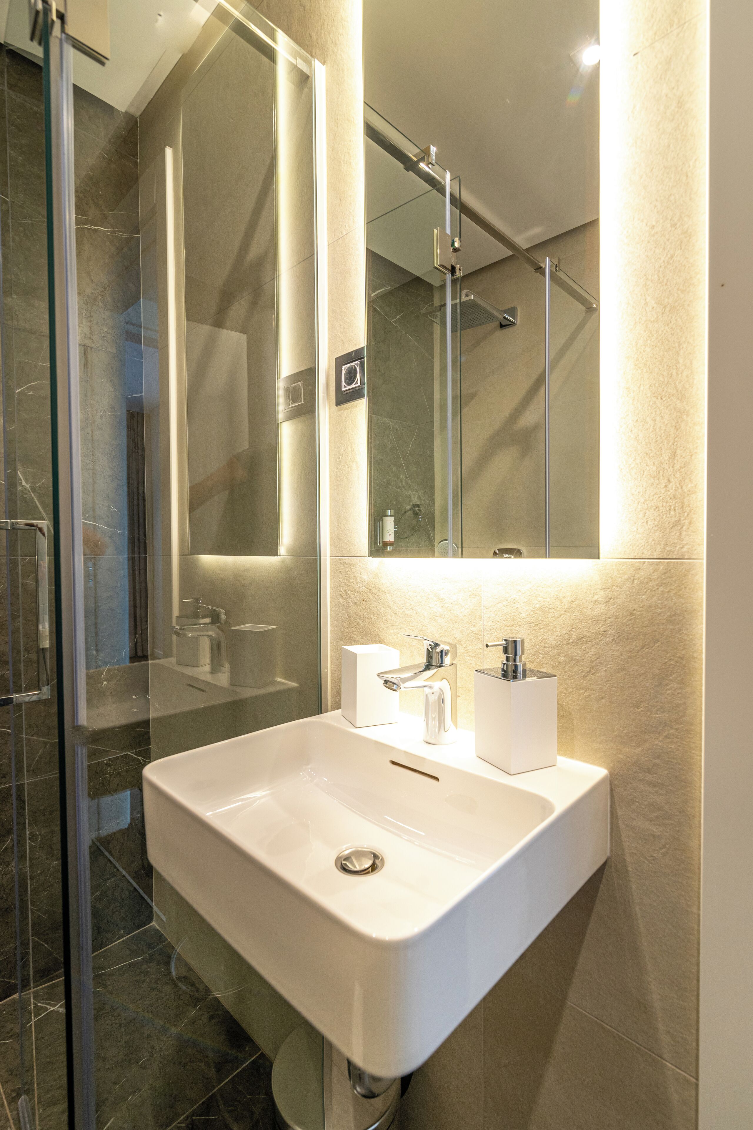 A modern bathroom with a glass shower enclosure, a white sink with a mirror above it, and a towel rack.