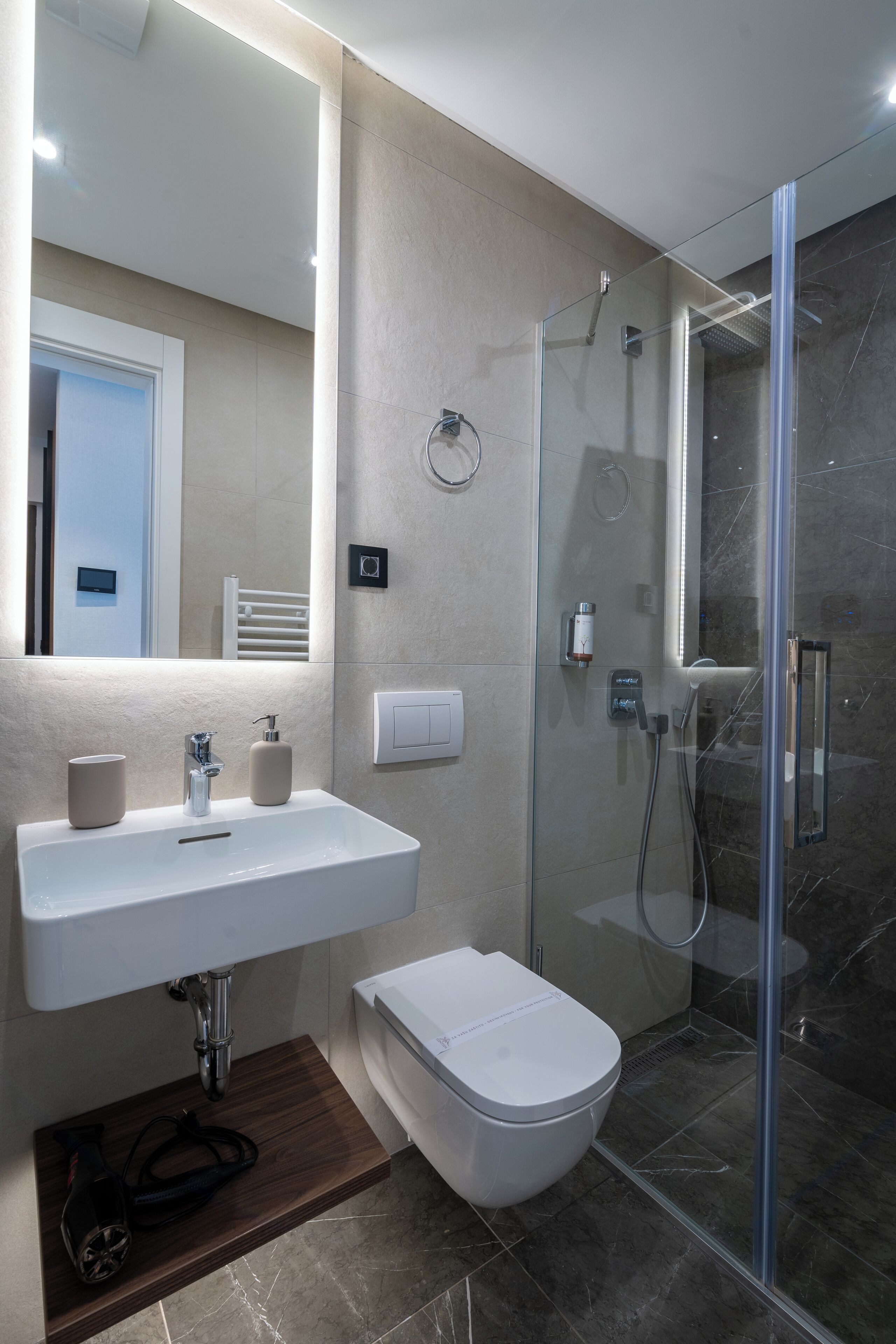 A modern bathroom with a glass-enclosed shower, a white sink with a mirror above it, and a toilet.