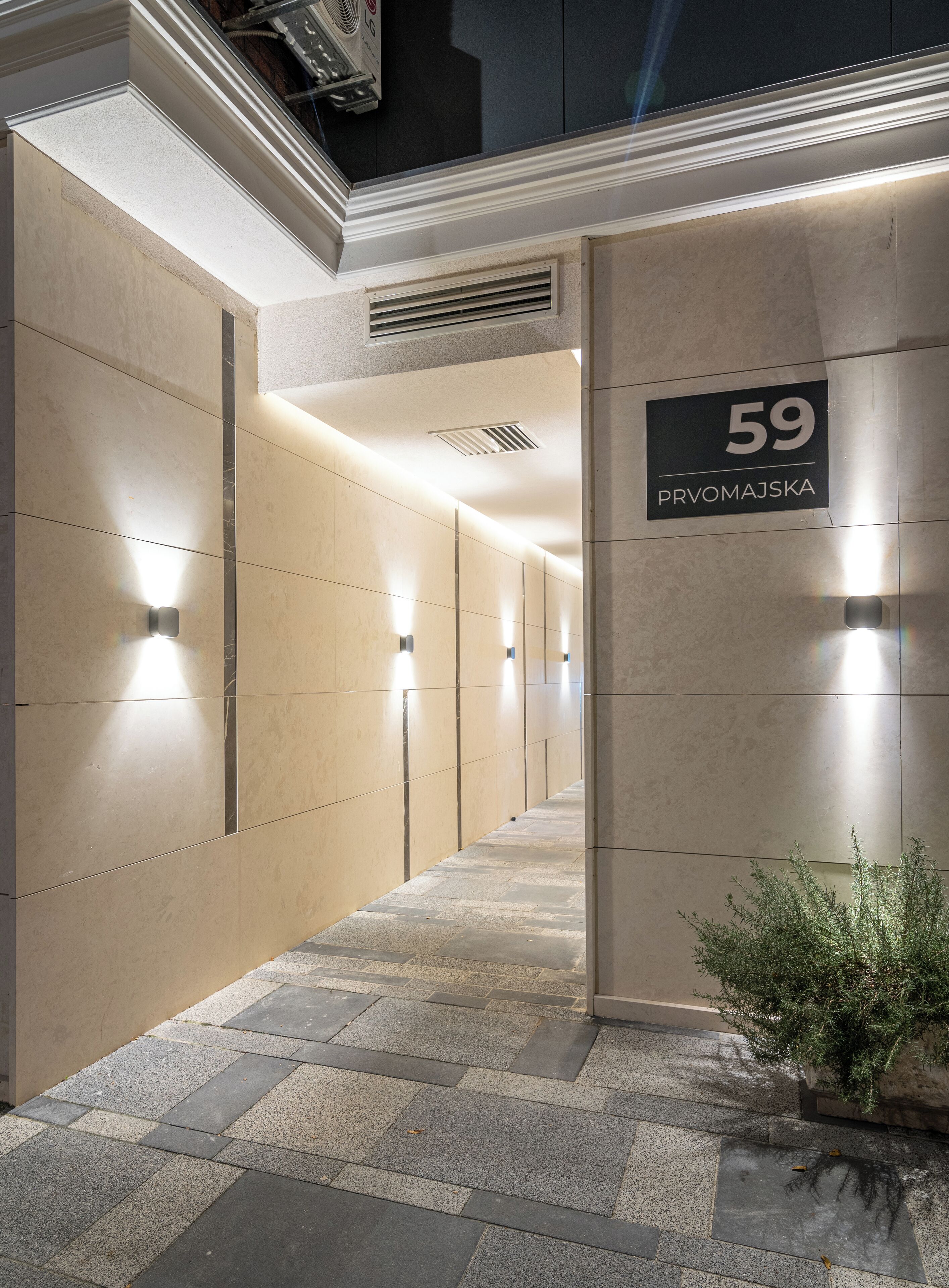 Un couloir avec une pancarte indiquant « 59 PRVOMAJSKA » et un pot de fleurs placé sur la droite.