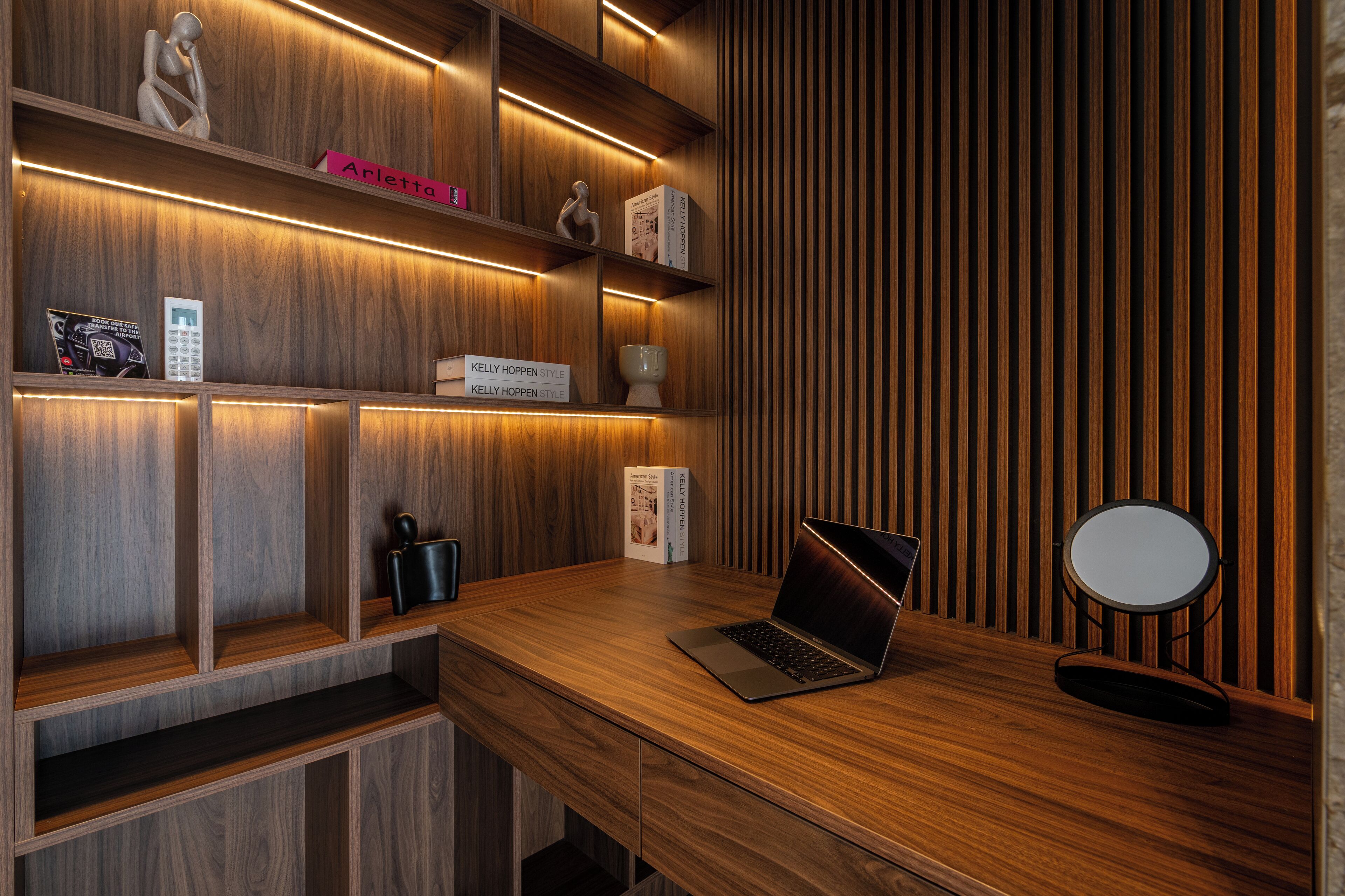 Een modern houten bureau met een laptop, boekenplanken en een kleine ronde spiegel.