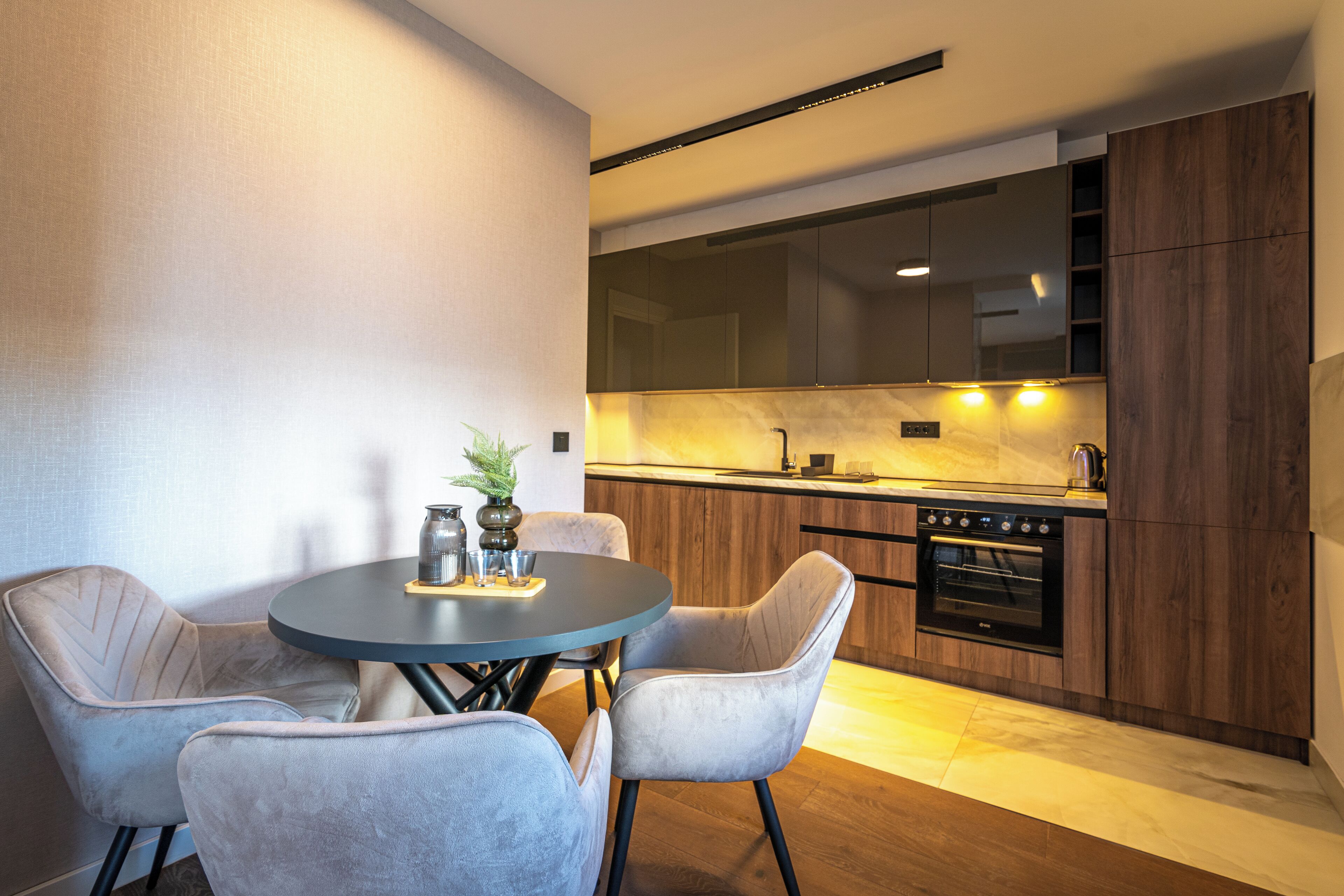 A modern kitchen with dark wood cabinets, a built-in oven, and a round dining table with four chairs.