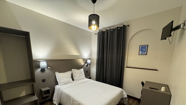 Quarto de hotel com cama, luminárias de cabeceira, televisão, escrivaninha e uma cadeira.