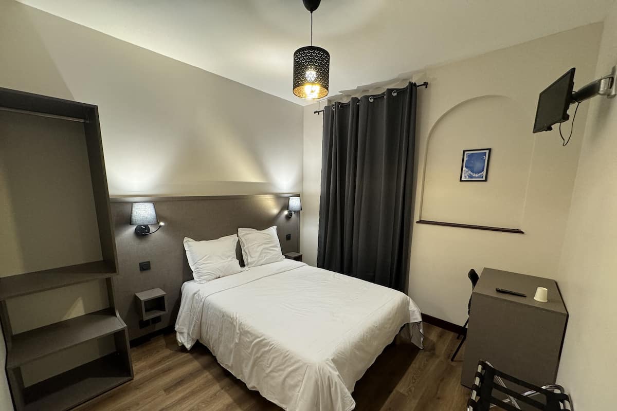A hotel room with a bed, bedside lamps, a TV, a desk, and a chair.