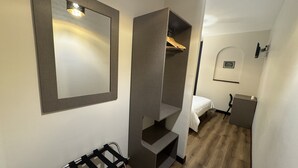 Quarto compacto com guarda-roupa, espelho, cama e uma pequena mesa.