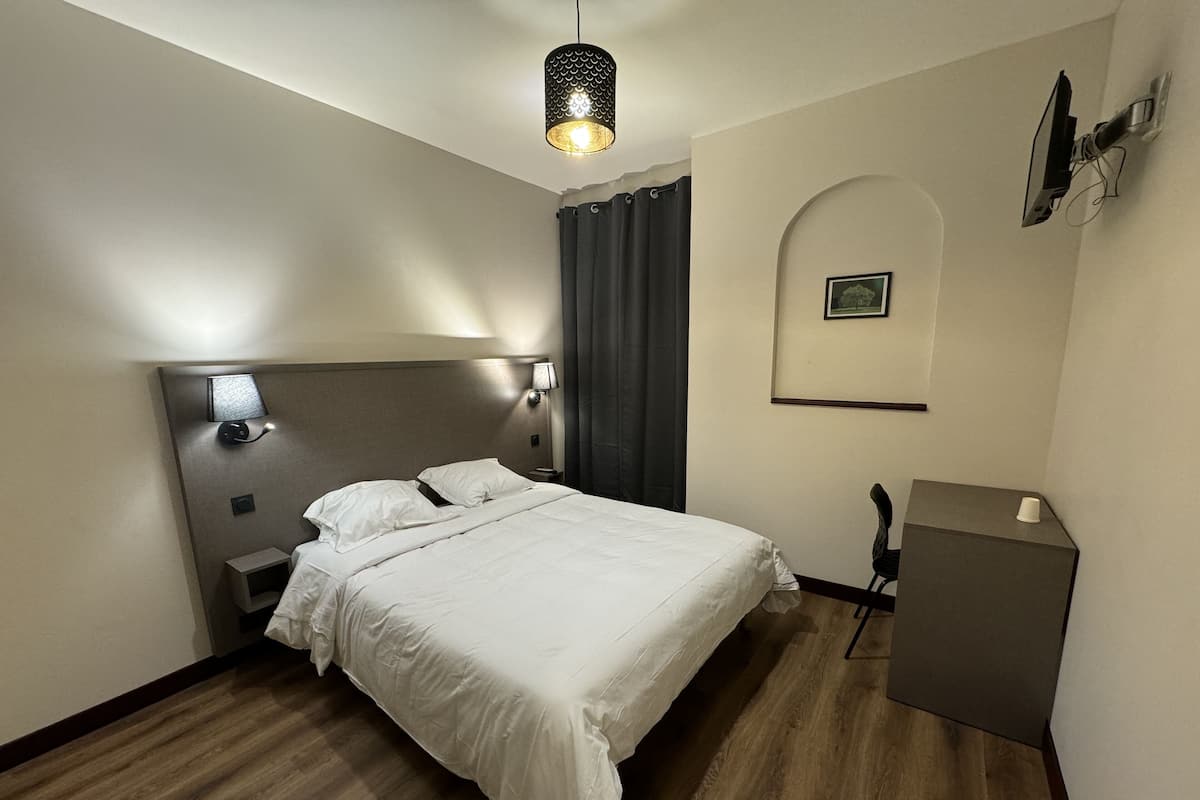 A hotel room with a large bed, a nightstand, a desk, and a hanging lamp.