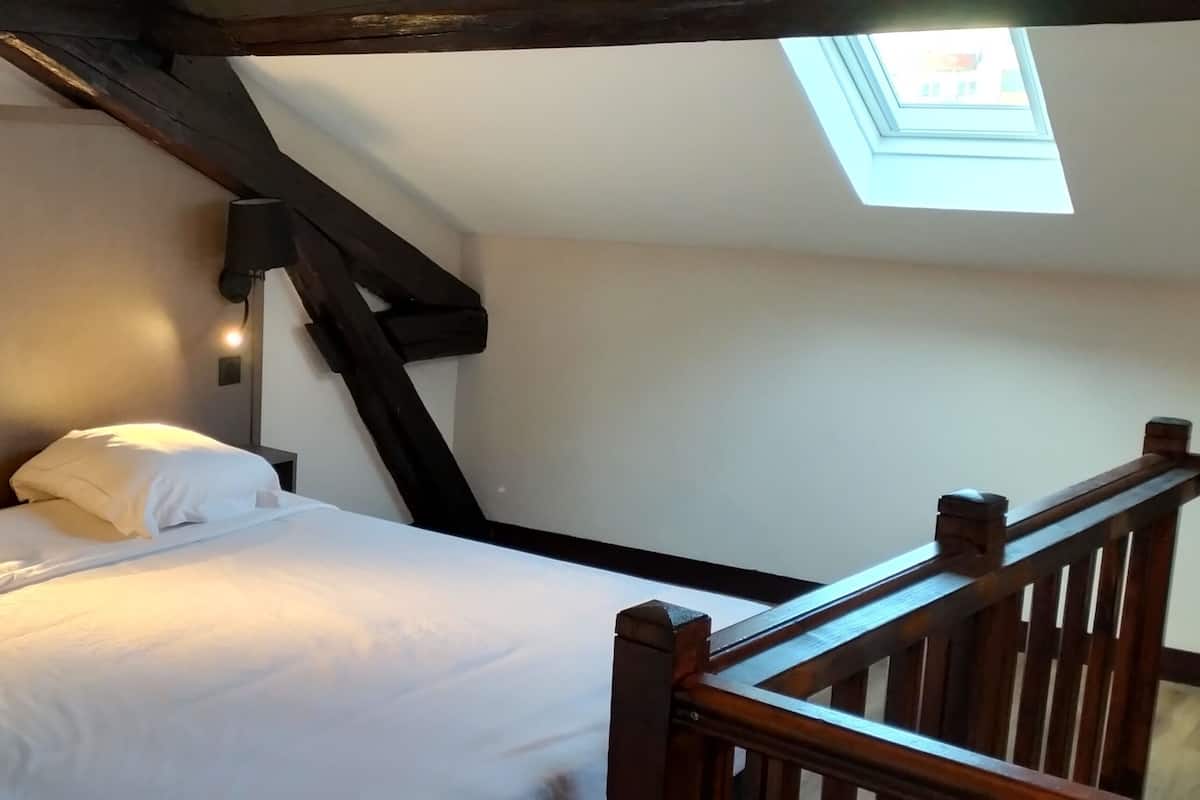A bedroom with a bed, a nightstand, a lamp, and a skylight.