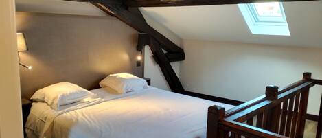 A bedroom with a bed, a nightstand, a lamp, and a skylight.