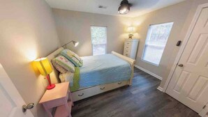 Une chambre à coucher comprenant un lit, une table de chevet, une lampe, une commode et des fenêtres.