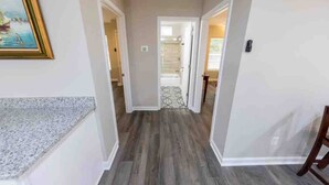 Un couloir doté d’un plancher en bois, de murs blancs et d’une porte donnant sur une salle de bain.