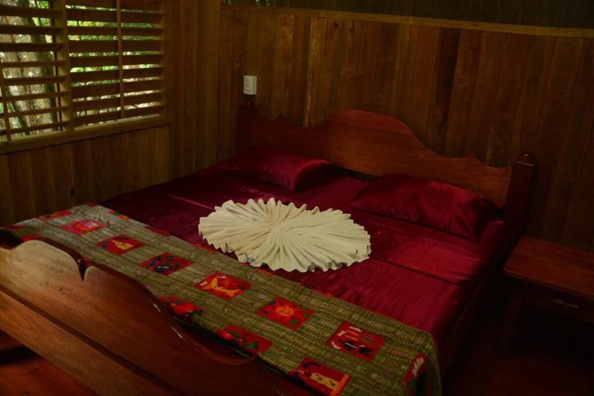 A wooden bed with a red bedspread and a quilt with a lion pattern.