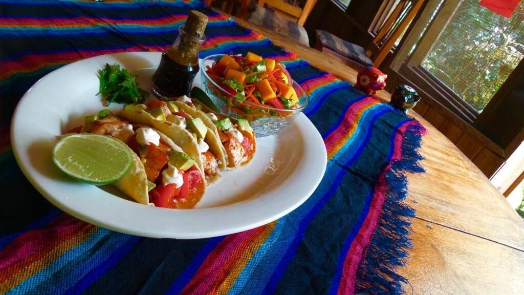 A plate of food with a lime wedge, a small bowl of salsa, and a bottle of hot sauce on a colorful tablecloth.