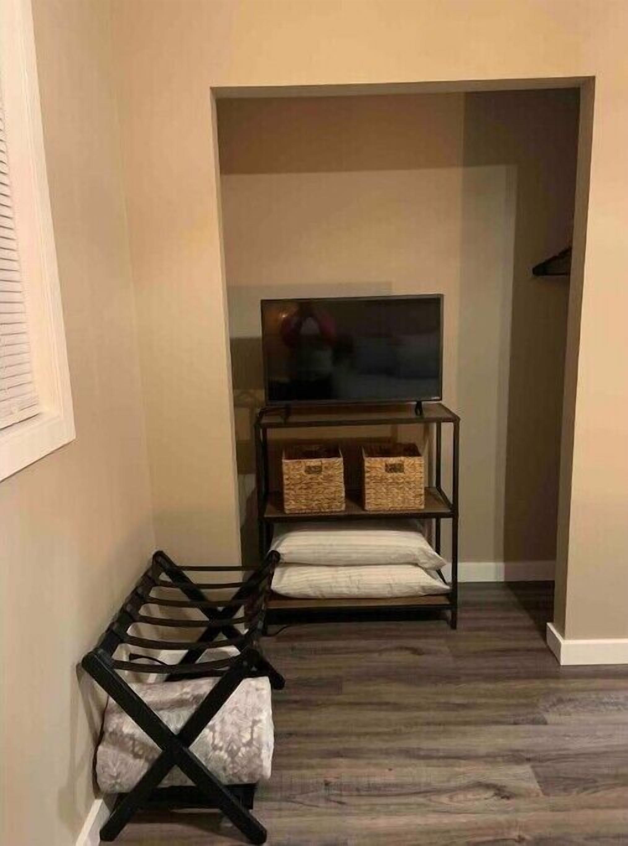 A narrow hallway with a wooden floor, a black metal rack with a folded blanket, and a TV on a shelf.