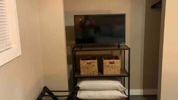 A narrow hallway with a wooden floor, a black metal rack with a folded blanket, and a TV on a shelf.