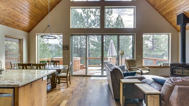 Een ruime woonkamer met een houten plafond, grote ramen, een schuifpui naar een terras en een gezellige zithoek.