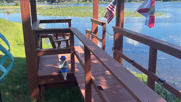 A wooden deck with a pergola, a swing, and a statue of a man playing a banjo.