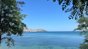 A coastal view with clear water, a sandy beach, and a distant hill with buildings. - Sinop Bahçeler Villa (Sinop)