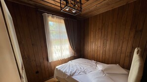 A bedroom with wooden walls, a bed with white linens, a window with sheer curtains, and a hanging light fixture. - Sinop Bahçeler Villa (Sinop)