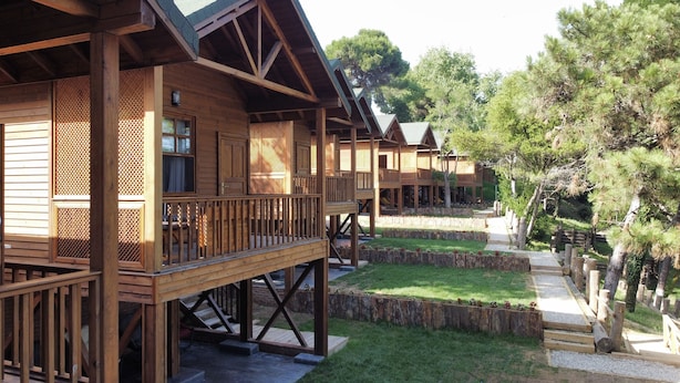 A row of wooden cabins with balconies, a grassy courtyard, and a wooden fence. - Sinop Bahçeler Villa (Sinop)