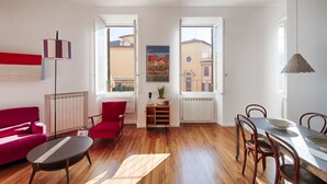 Ein heller Wohnraum mit einem roten Sofa, einem Holztisch, einem Esstisch mit Stühlen und einem Gemälde an der Wand.