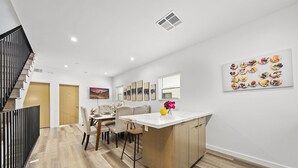 Een moderne keuken met een centraal eiland, houten vloeren en een eethoek met stoelen en een tafel.