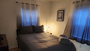 Ein Schlafzimmer mit einem Bett, Vorhängen, einer Nachttischlampe und einem gerahmten Bild an der Wand.