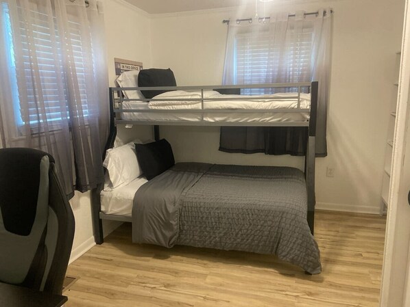 Habitación con literas, escritorio, silla, cortinas y un cartel en la pared.