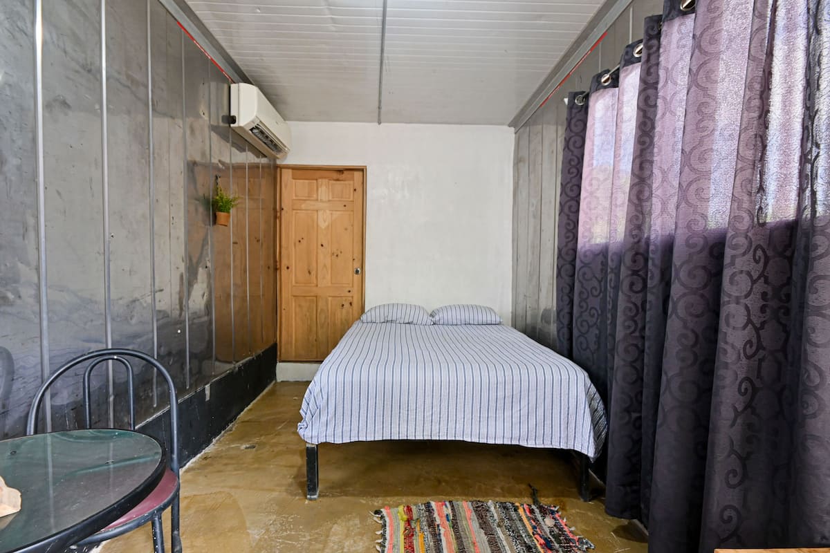 Un dormitorio con cama, una silla, una mesa, cortinas y una puerta.