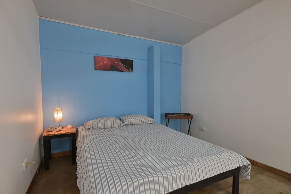 Un dormitorio con cama, mesita de noche, lámpara y una pequeña mesa.