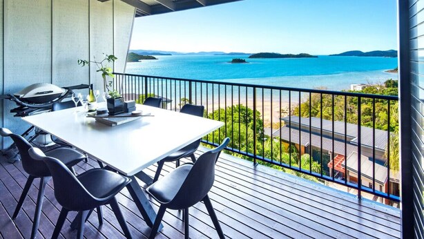 Un balcon avec une table et des chaises, donnant sur une étendue d’eau et sur de la verdure.