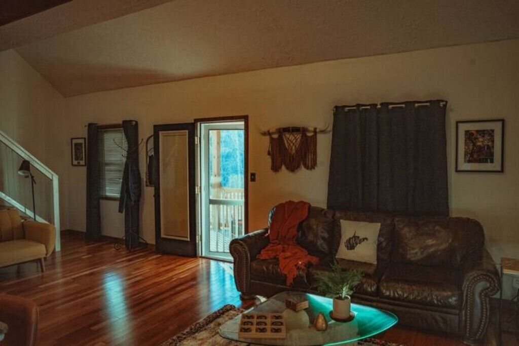 Una sala de estar con un sofá de cuero marrón, una mesa de centro con una planta y una puerta que da a un balcón.