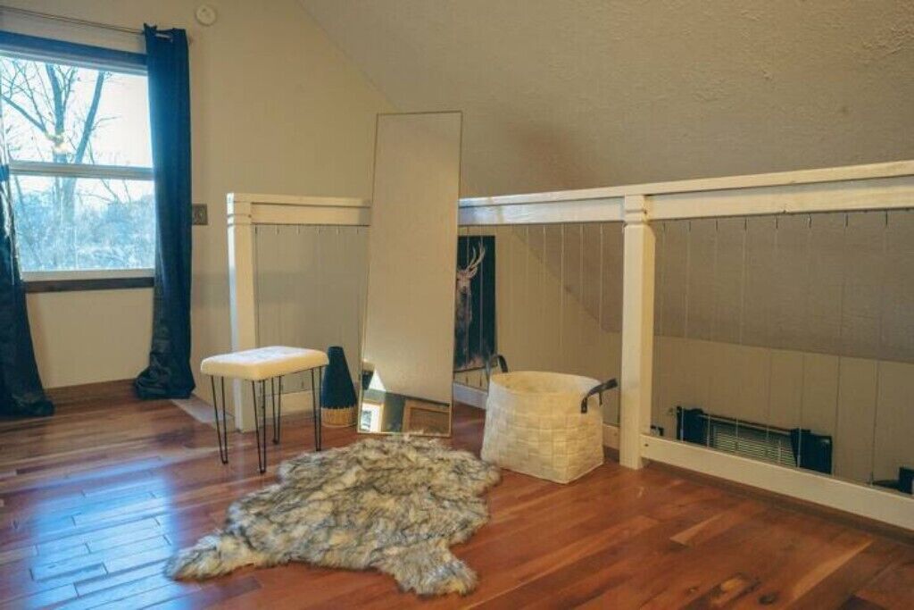 Una habitación con suelo de madera, alfombra de piel, un banco, un espejo y un radiador.