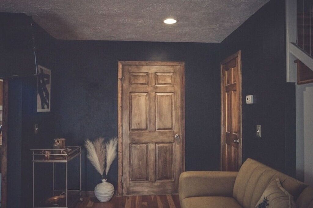 A room with a wooden door, a sofa, and a small table with a vase.