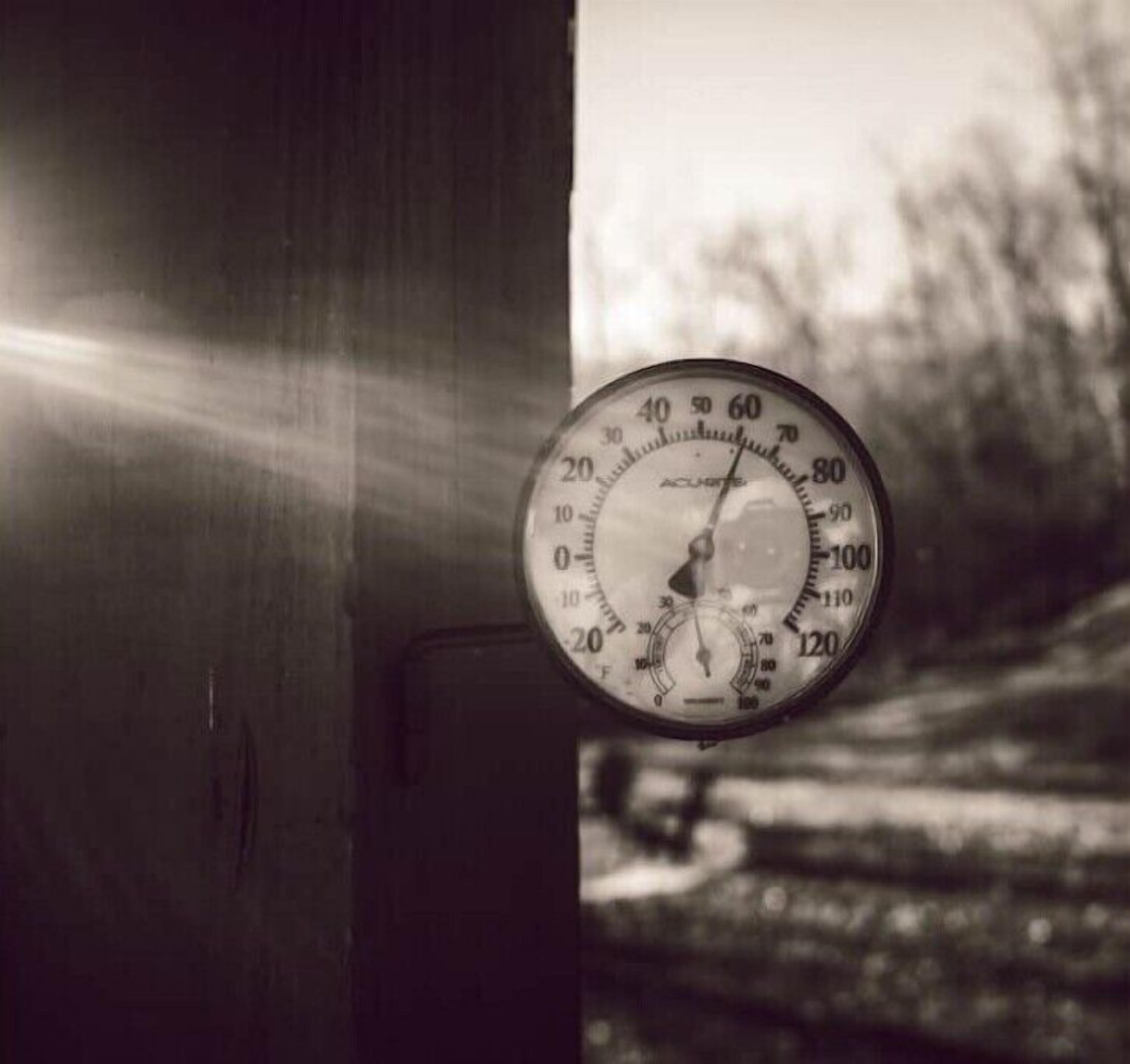 Een snelheidsmeter bevestigd aan een houten constructie, mogelijk een deur of muur, met een vage achtergrond die een buitenshuis omgeving doet vermoeden.