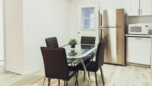 Een kleine keuken met een eettafel met glazen blad, vier stoelen, een koelkast, een magnetron en een vaatwasser.