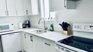 Een moderne keuken met witte kasten, een roestvrijstalen spoelbak, een magnetron, een koffiezetapparaat, een afwasmiddeldispenser en een fornuis.