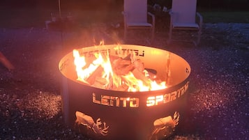 A fire pit with "LEITO SPORTING" branding, surrounded by gravel and two white chairs.