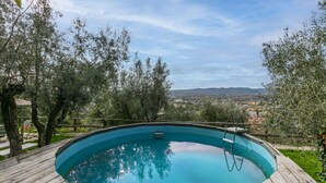 Eine Holzterrasse mit einem runden Pool, umgeben von Bäumen und Blick auf eine Stadtlandschaft.