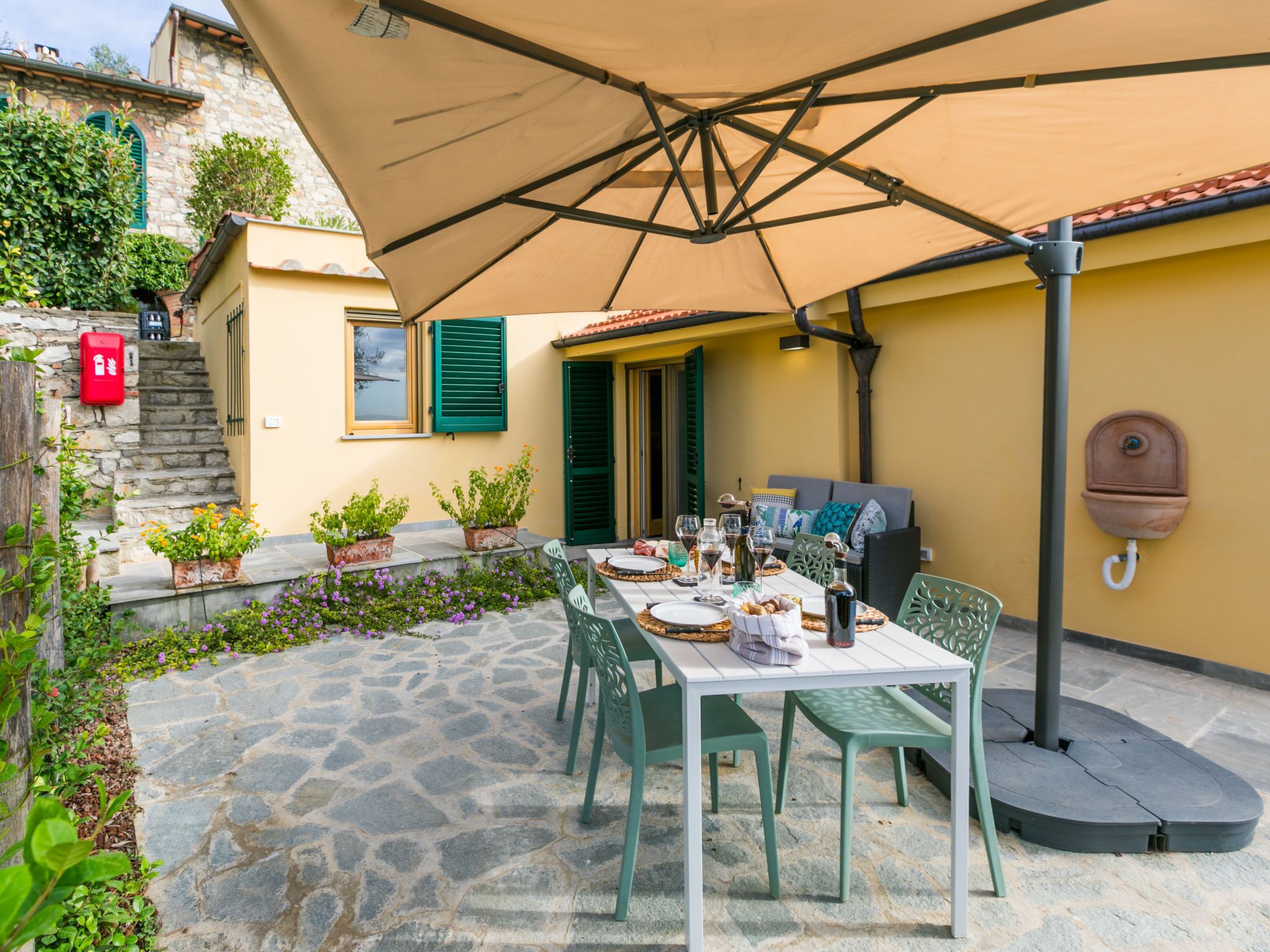 An outdoor patio with a table set for dining, surrounded by stone flooring and potted plants.