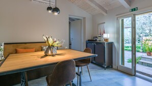 Ein Essbereich mit einem Holztisch, zwei Stühlen, einer Pflanze in einer Vase, einer Bank, einem Schrank und einer zur Außenwelt führenden Tür.