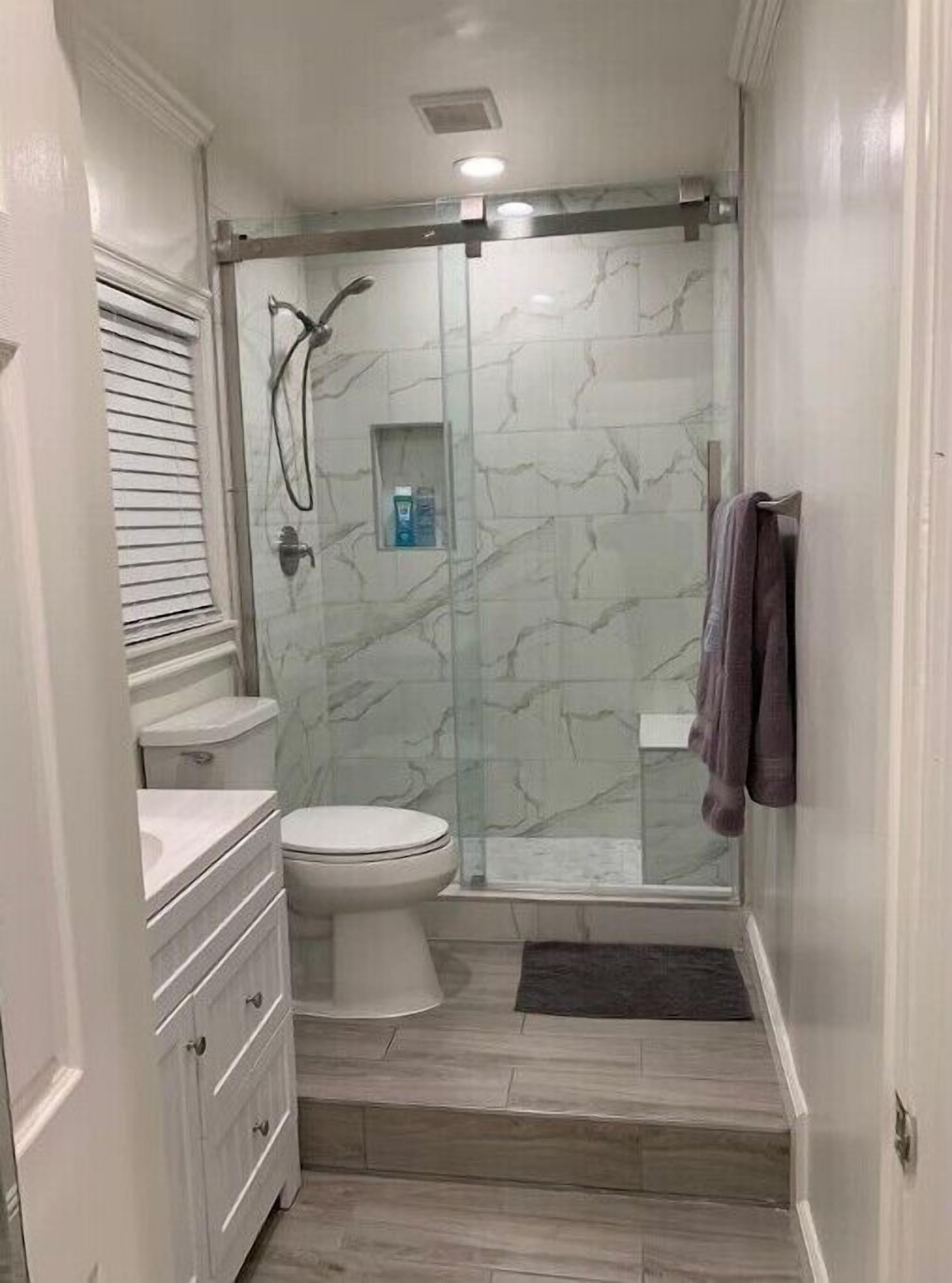 Un baño con ducha de vidrio, inodoro y tocador con cajones.