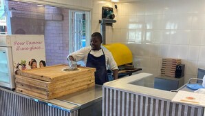 Una zona de cocina con una persona preparando comida, una pared de ladrillo, un horno amarillo y un cartel con texto en francés.