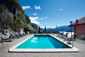 Una piscina rectangular con agua azul cristalina, rodeada de sillas de descanso y una terraza de ladrillo.