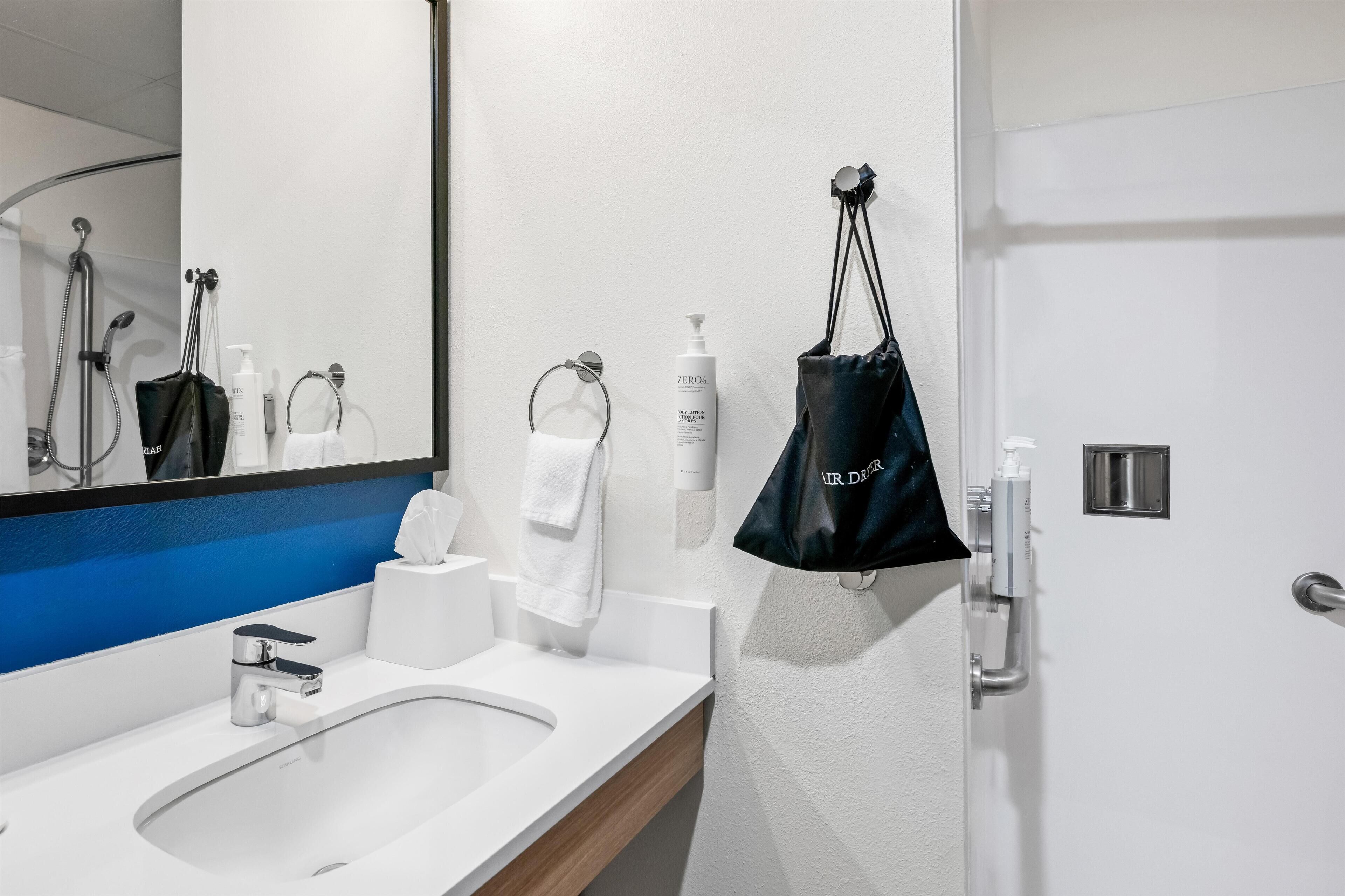 A modern bathroom with a sink, mirror, towel rack, and toiletries.