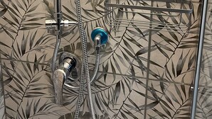 A shower with a bamboo leaf pattern on the wall, a handheld showerhead, and a wall-mounted faucet. - House Caracciolo (Naples)