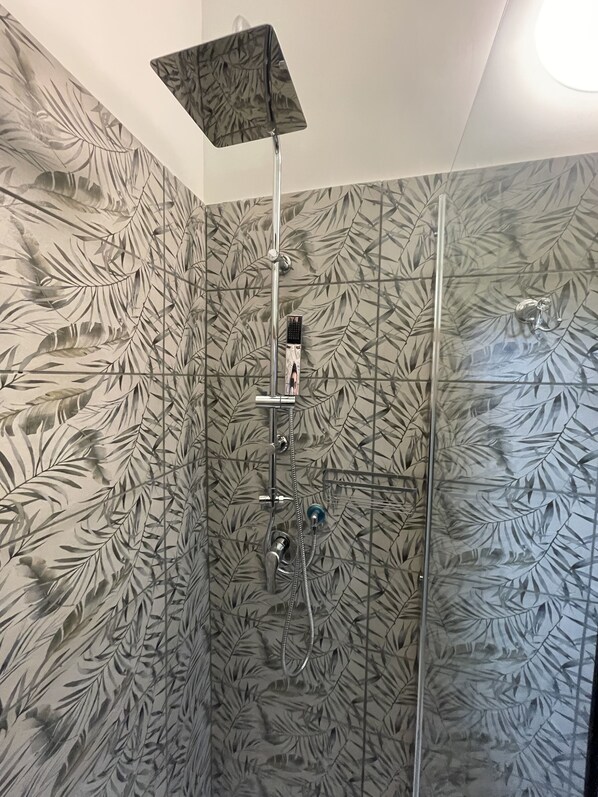 Une douche avec une porte en verre et un mur décoré de motifs de feuilles.
